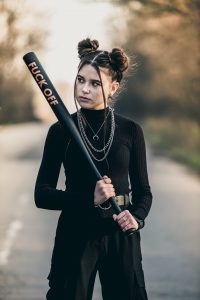 schwarz gekleidetes Mädchen hält eine Baseball -Keule mit dem Aufdruck "Fuck Off" zu Schlag bereit