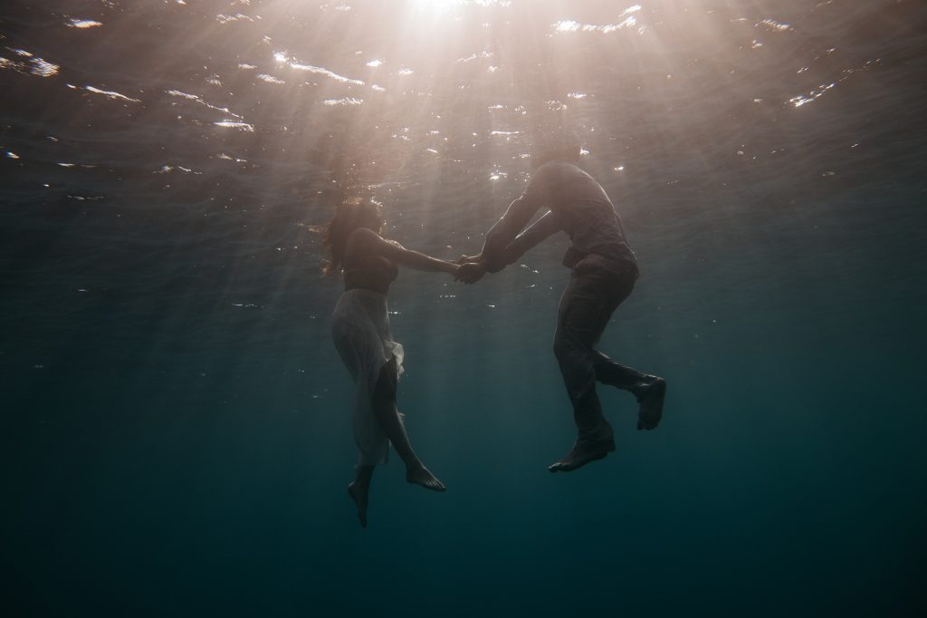ein Paar unter Wasser hält sich an den Händen und taucht gleich auf